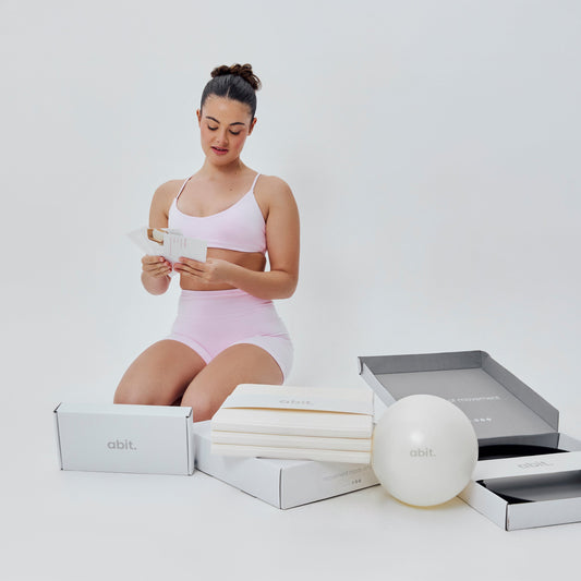 Woman sitting with abit.of home Pilates kit including mat, Pilates ball and accessories